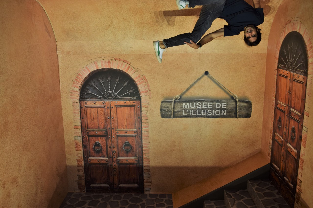 Une visiteuse marche au plafond dans le décor de cour lyonnaise du Musée de l'Illusion · Photo Steven Carnel